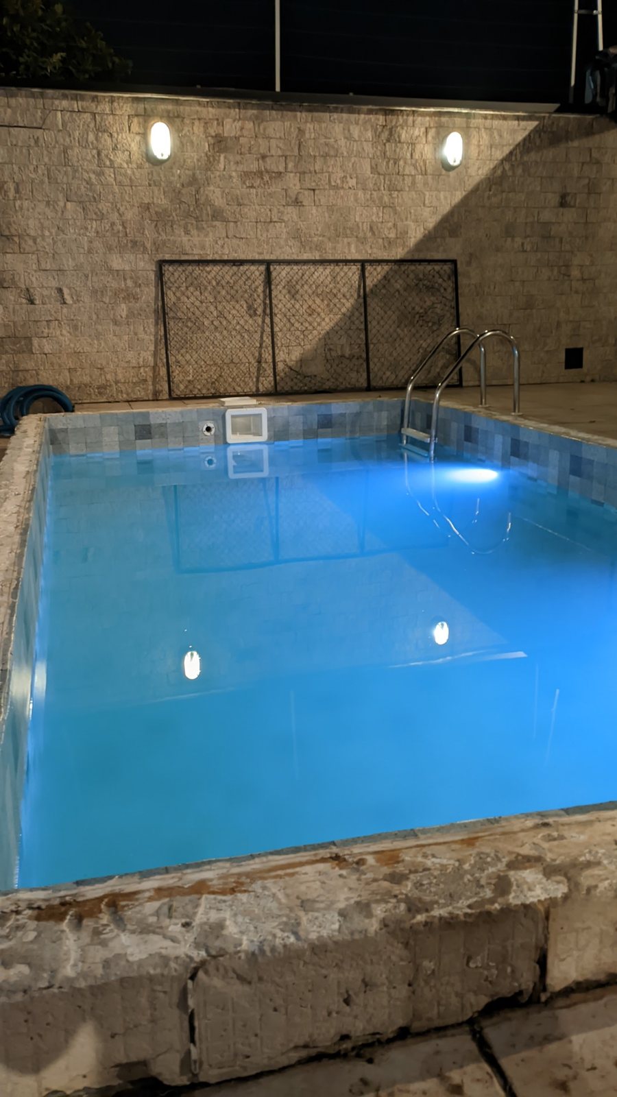Piscina de alvenaria à noite, com escada e luzes