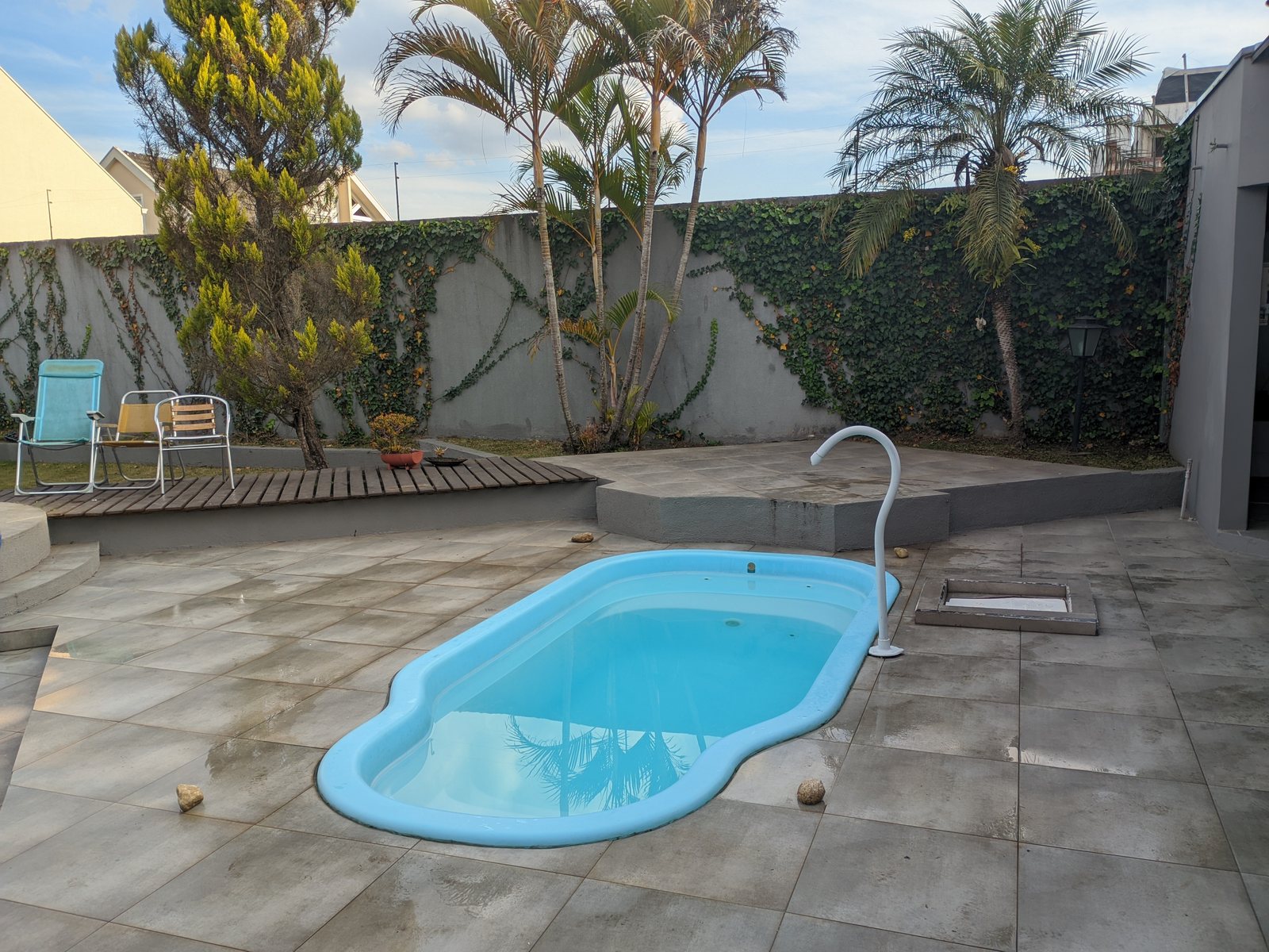 Piscina de fibra com água clara, palmeiras e cadeiras