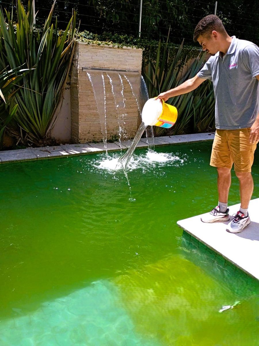 Técnico aplicando tratamento em piscina com a água verde e uma cascata ao fundo